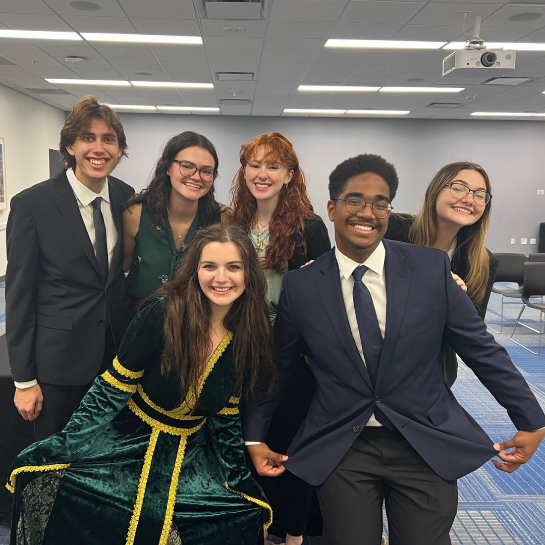 Group of team members at the UF Charity tournament who are all smiling together while two competitors in the front are doing a curtsey 